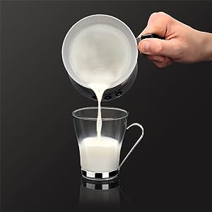 Mano vertiendo leche de una jarra de cerámica blanca a una taza de vidrio transparente