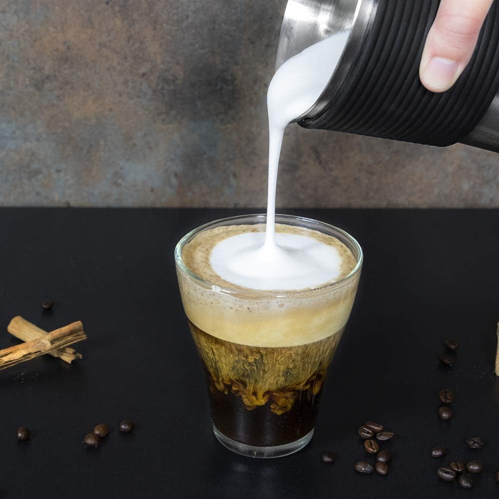 Una taza de café con leche sobre una superficie negra con granos de café y canela