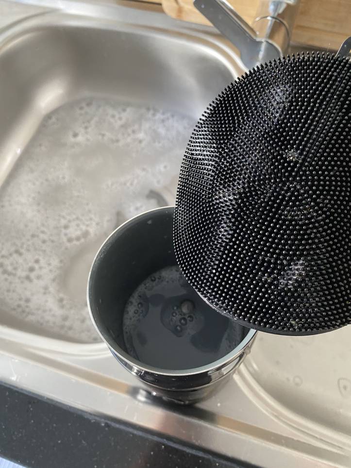 Colador negro que se enjuaga en un fregadero con agua jabonosa.